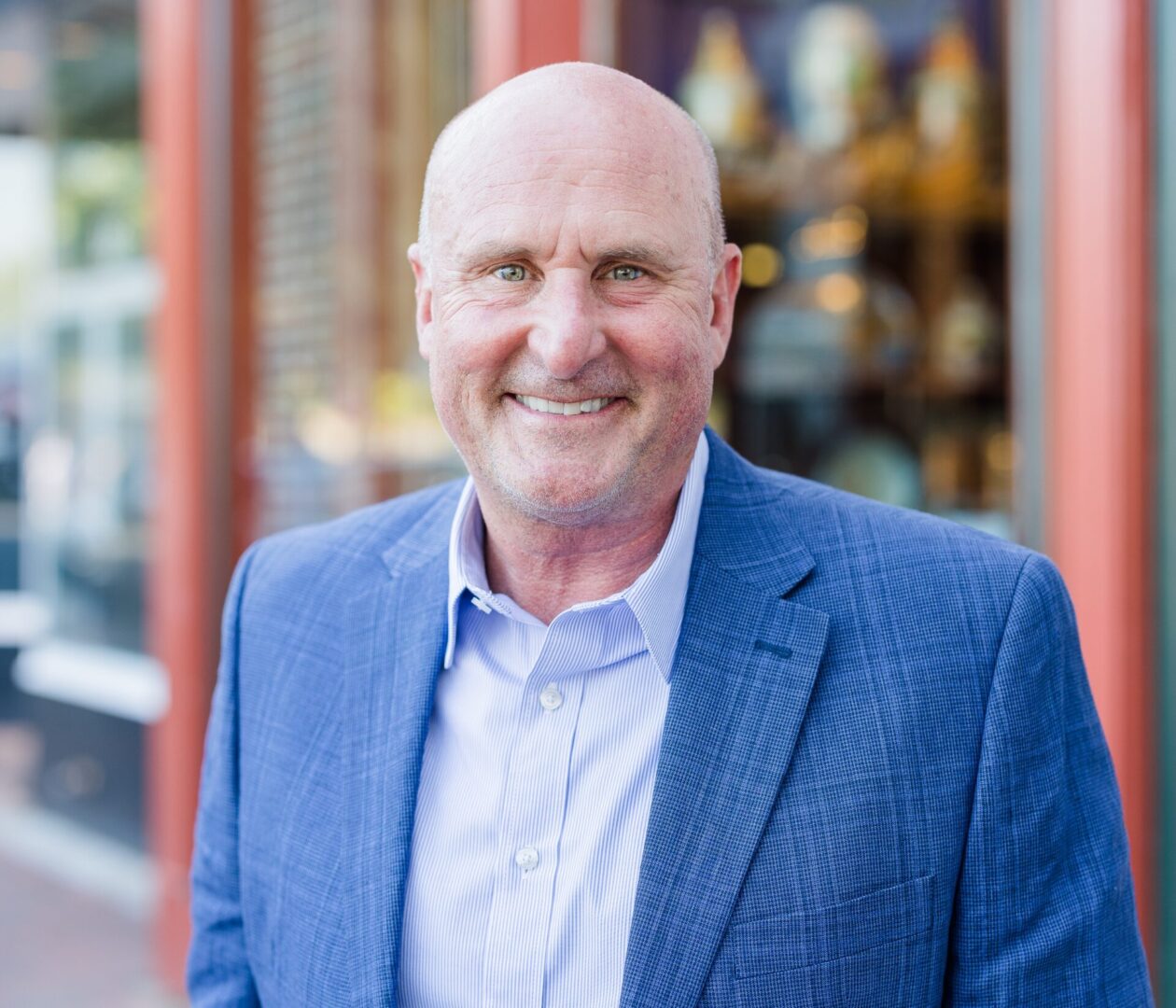 Smiling bald man in a blue blazer standing outdoors.