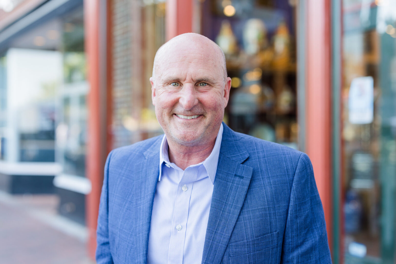 Smiling bald man in a blue blazer outdoors.